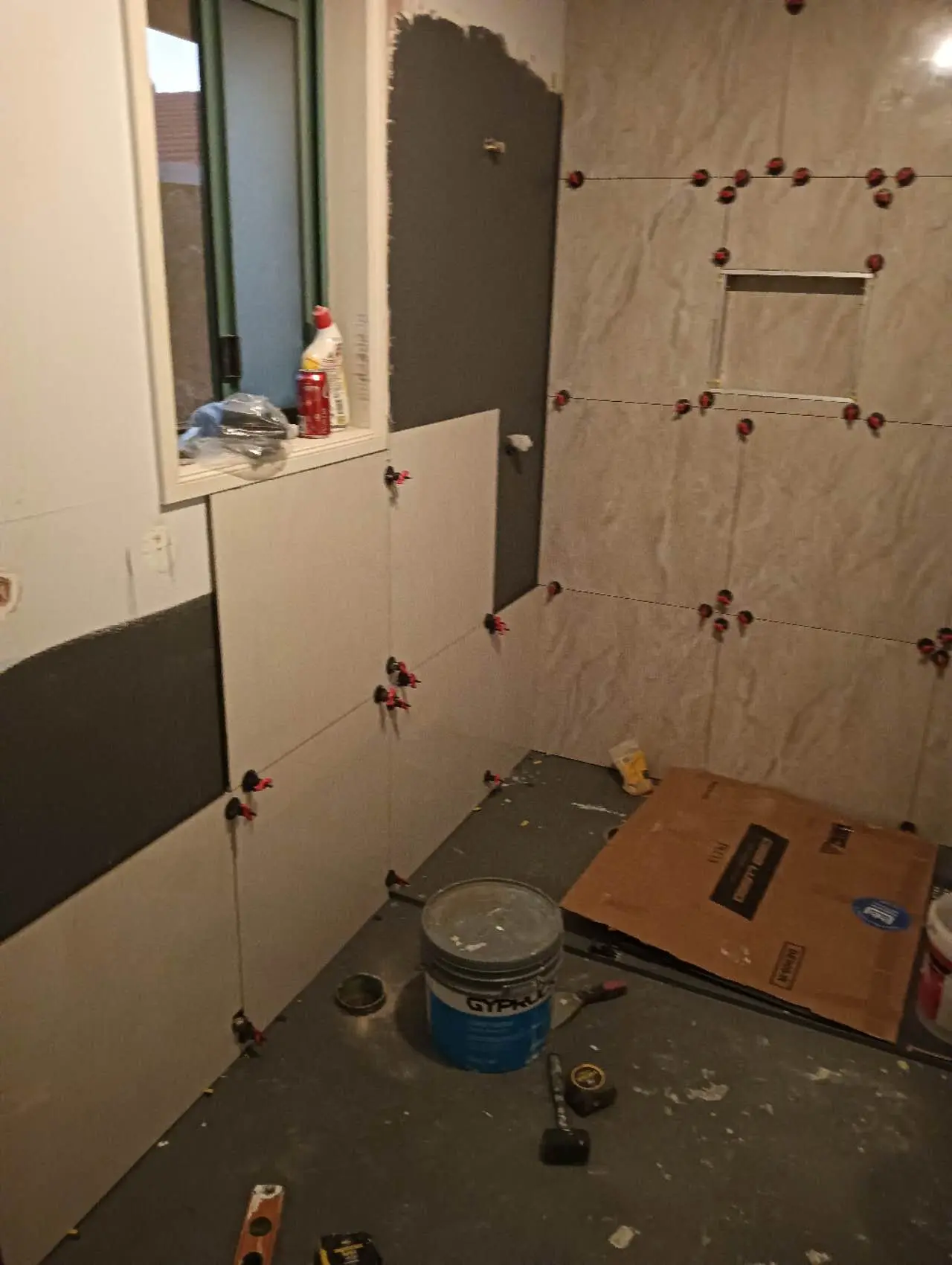 Large-format bathroom wall tiles being levelled around a recessed shower niche