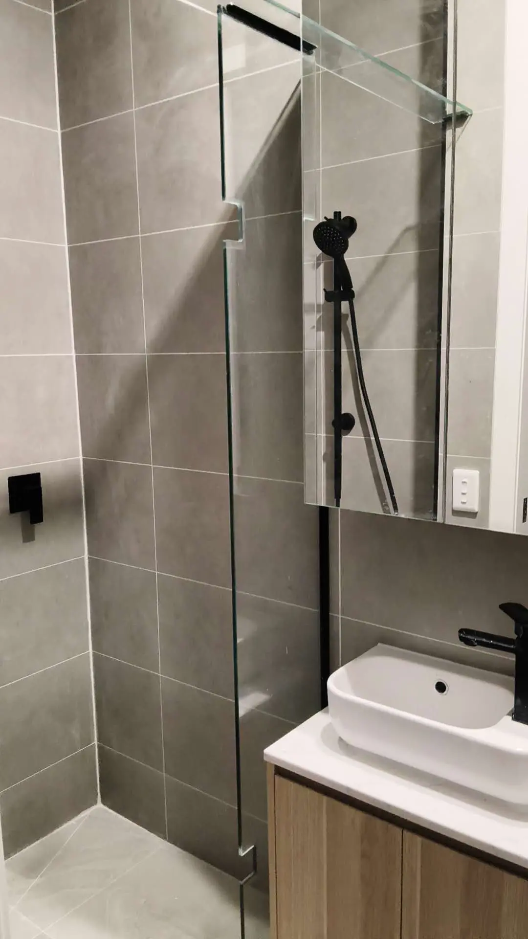 Compact bathroom with glass shower screen, grey tiles and black fittings